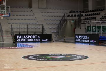 Vista dell'interno del palazzetto con tribune e pavimento in legno con logo del Comune di Gravellona Toce